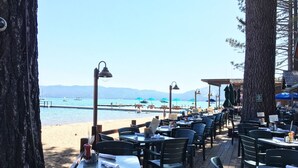 Zona de menjador a l'aire lliure amb taules i cadires, amb vista a una platja i al mar.