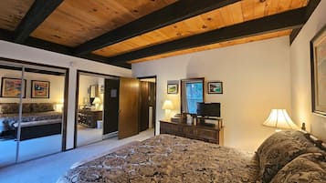 A bedroom with a large bed, wooden ceiling beams, a dresser, a television, and framed artwork on the walls.