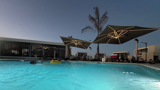 Een zwembad met helderblauw water, omringd door ligbedden en parasols.