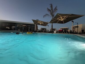 Ein Schwimmbecken mit klarem, blauem Wasser, umgeben von Liegestühlen und Sonnenschirmen.