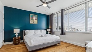 Ein Schlafzimmer mit Bett, Deckenventilator, Fenster mit Jalousien und einem Bild an der Wand.