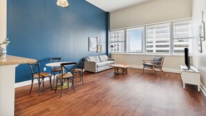 Un salon moderne avec un mur d’accent bleu, un plancher en bois, un canapé gris, une table basse et un coin repas avec des chaises.