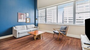 Un salon avec un mur d’accent bleu, un canapé gris, une table basse en bois et une chaise en bois.