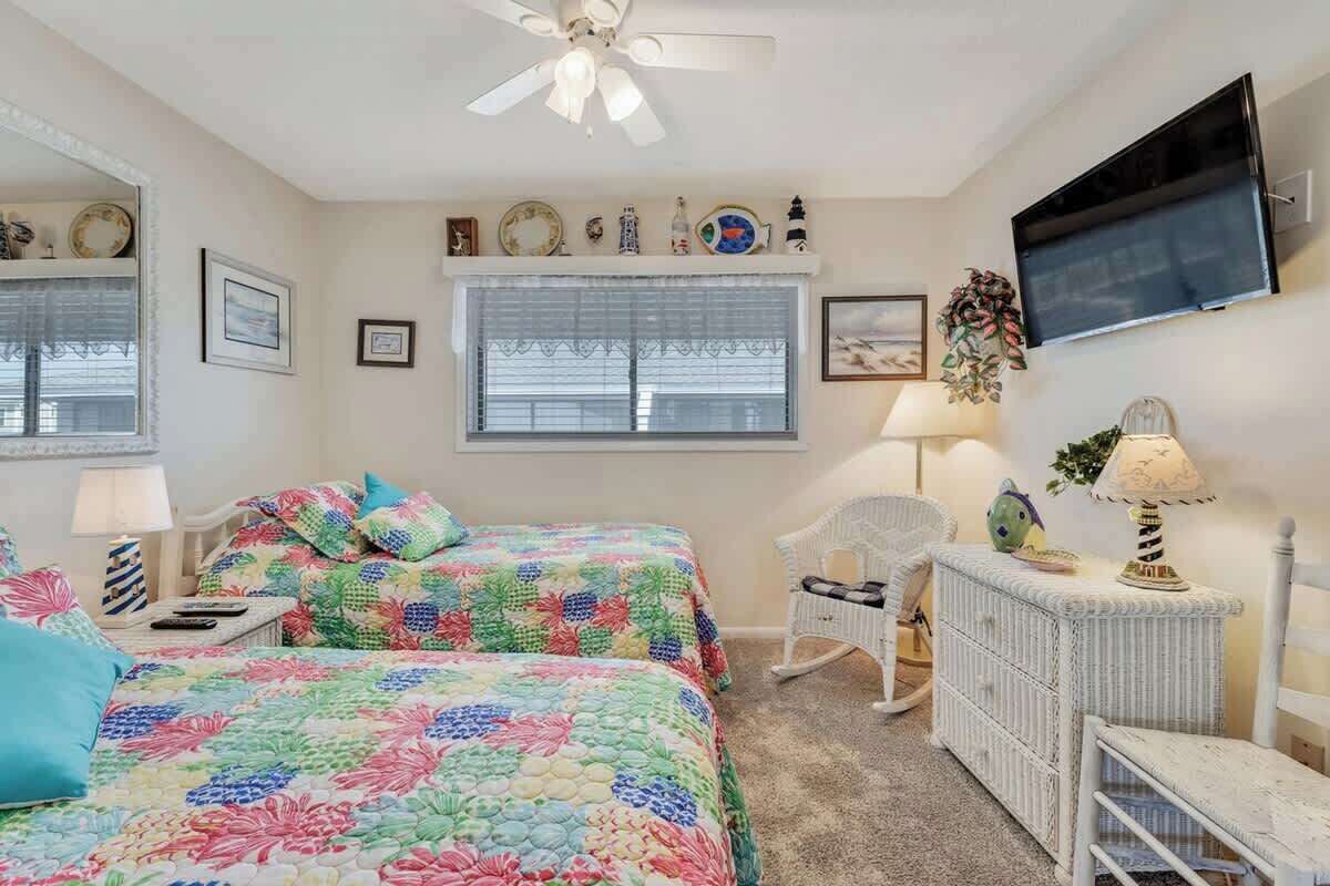 Une chambre avec deux lits, un ventilateur de plafond, une télévision et une fenêtre avec des stores.