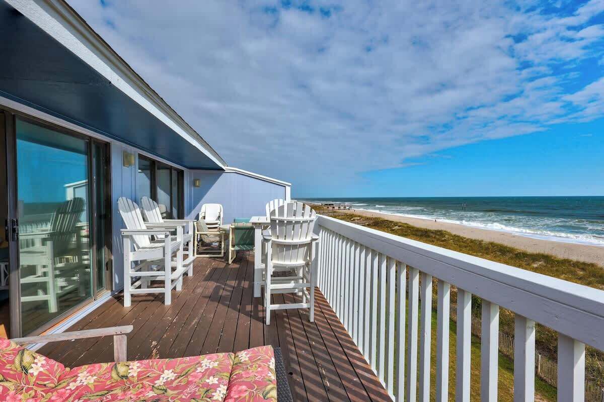Um deck de madeira com cadeiras e uma mesa brancas, com vista para o oceano.