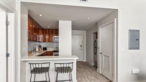 Une cuisine moderne avec des meubles blancs, un îlot central doté de deux tabourets de bar et une porte visible donnant sur une autre pièce.