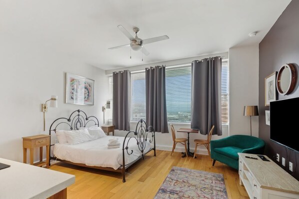 Une chambre moderne comprenant un lit, un bureau, une chaise, un téléviseur et un ventilateur de plafond.