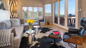 A spacious living area with a sofa, coffee table, and a chair. There is a large window providing a view of the outdoors.