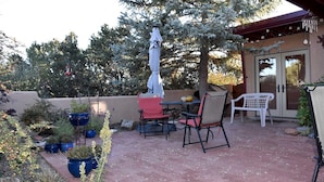 Un patio al aire libre con una mesa y sillas, rodeado de plantas en macetas y un árbol.