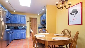 Una cocina compacta con armarios azules, una mesa de comedor con cuatro sillas y piso de baldosas.