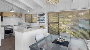 A modern kitchen with white cabinetry, stainless steel appliances, and a glass dining table. - Seaview Family Haven - Pauanui Holiday Home (Pauanui)