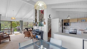 A modern kitchen with white cabinets, a dining area with a glass table, and a view of the outdoors. - Seaview Family Haven - Pauanui Holiday Home (Pauanui)