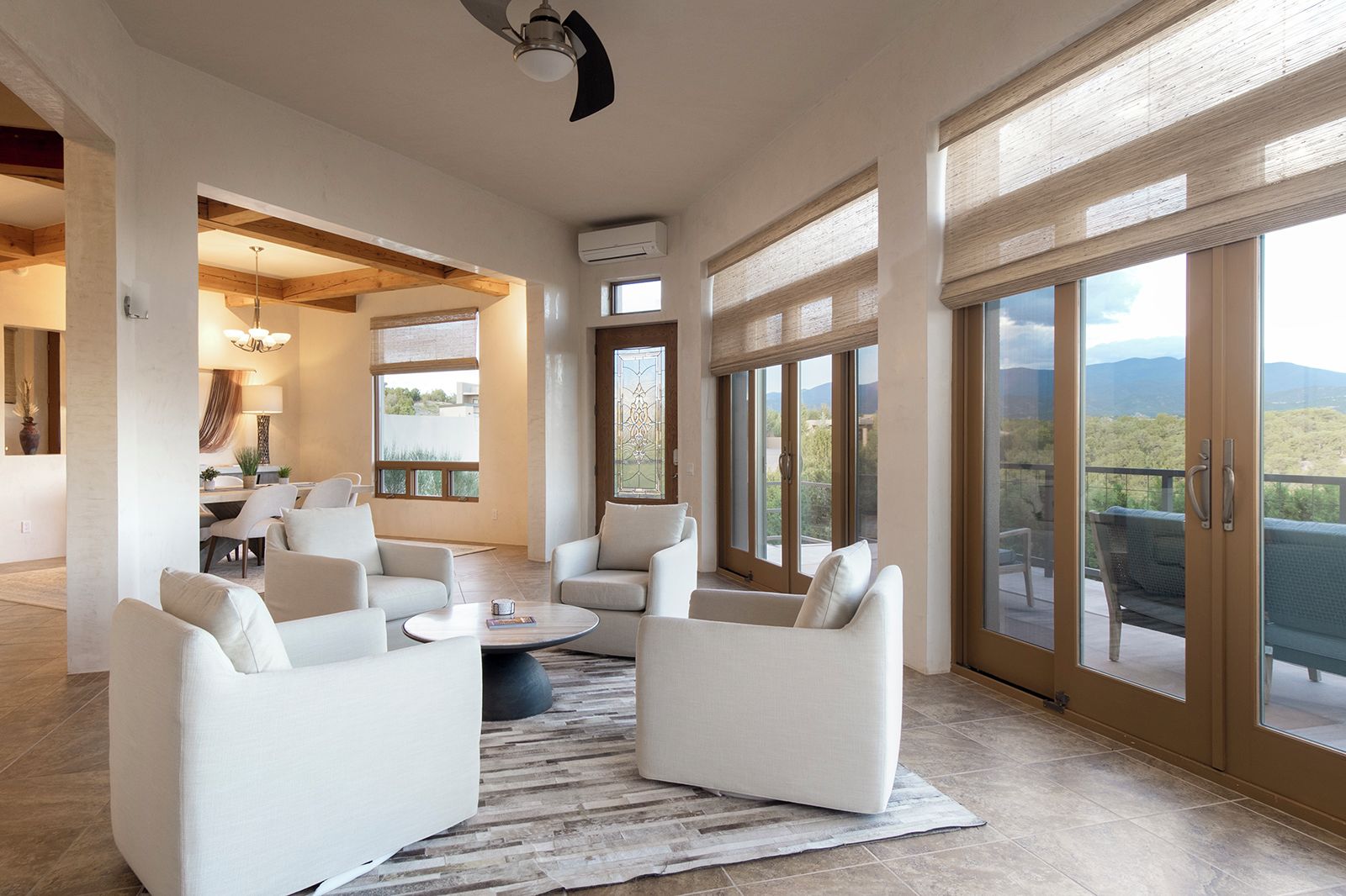 A spacious living area with a round coffee table, white sofas, and a view of the outdoors through large sliding glass doors.