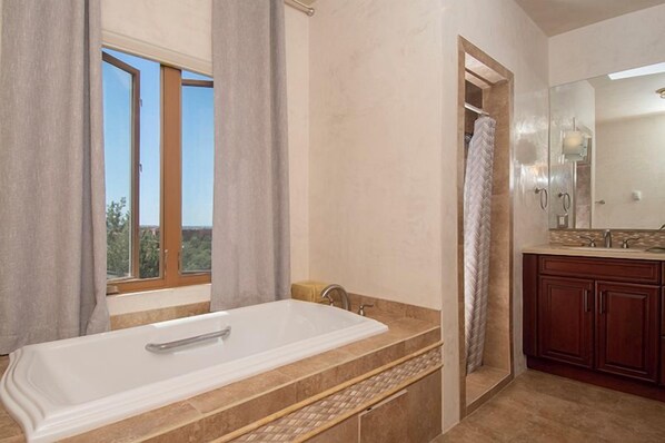 A bathroom with a large bathtub, a shower, and a vanity with a mirror.
