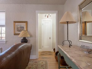 Une pièce avec un canapé en cuir marron, une lampe, un miroir et une porte donnant sur une autre pièce.