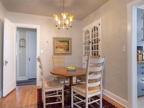 A dining area with a round table, four chairs, a chandelier, and a door with glass panels.
