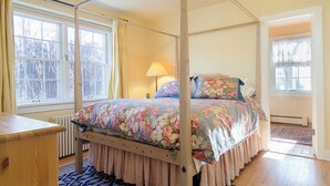 Un lit à baldaquin avec une literie à motifs floraux, une table de chevet en bois et une fenêtre avec des rideaux.