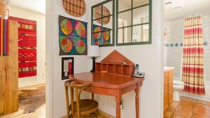 Baño con ducha, inodoro y lavamanos. Hay un taburete de madera y una mesa con teléfono.