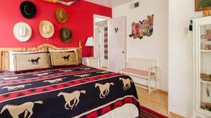 Un dormitorio con una cama, un ventilador de techo, una pared con sombreros y una puerta.