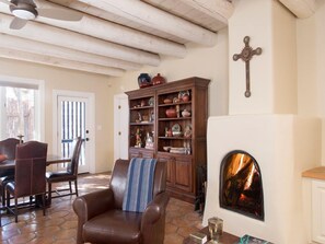 A cozy living room with a fireplace, a leather armchair, a wooden cabinet with decorative items, and a cross on the wall.