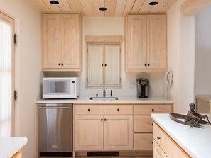 A compact kitchen with wooden cabinets, a microwave, a coffee maker, and a sink.