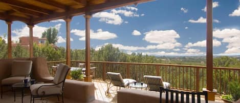 Un espacio de estar al aire libre techado con sillas y mesas, con vistas a un paisaje con árboles y una vista distante.