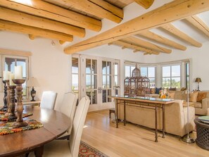 Un'ampia stanza con soffitto in legno, un tavolo da pranzo con sedie, un divano e una vista attraverso ampie finestre.