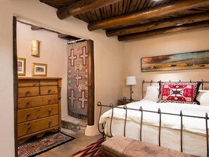 Un dormitorio con cama, cómoda de madera, alfombra estampada y un cuadro en la pared.