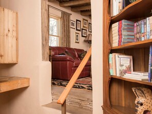 Una sala de estar acogedora con un sofá de cuero rojo, una estantería de madera y una escalera que sube a otro nivel.