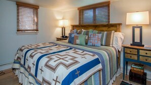 A bedroom with a large bed, two bedside tables, a nightstand, and a window with blinds. - Definitely Downtown in Santa Fe (Santa Fe)