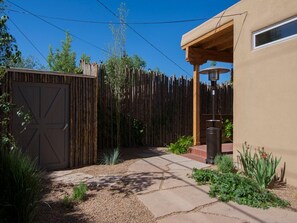 A fenced backyard with a wooden gate, a concrete pathway, and a patio area with a lamp post.