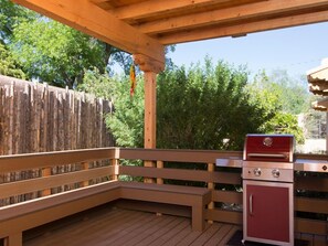 Un patio exterior con cubierta de madera, una parrilla y un refrigerador pequeño.