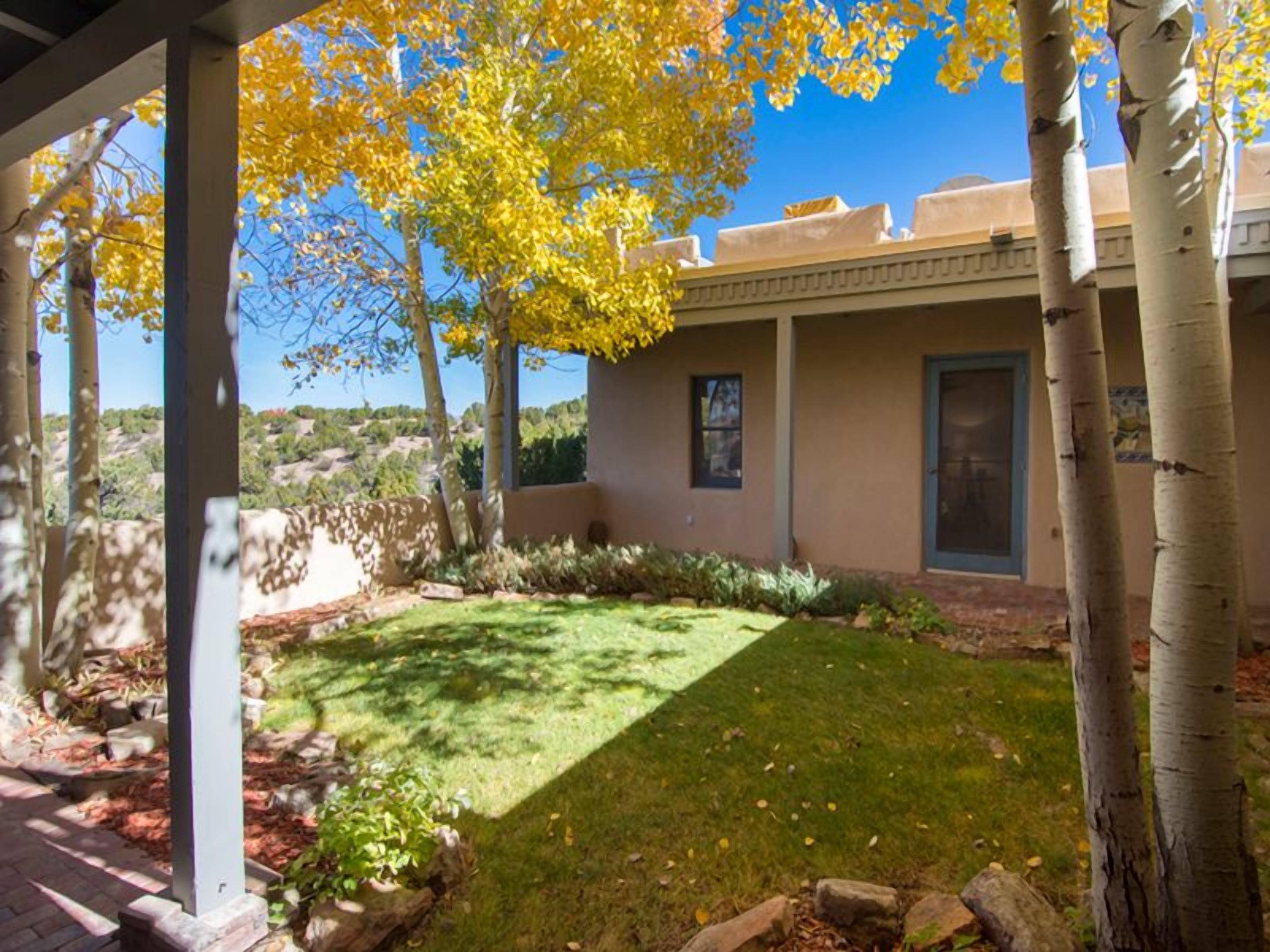 A covered patio area with a lawn, trees, and a building with a flat roof.