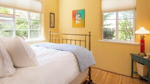 Ein Schlafzimmer mit einem Bett, zwei Fenstern mit Jalousien, einem Deckenventilator und einem Nachttisch mit einer Lampe.