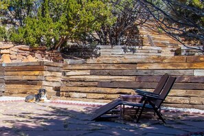 A wooden bench and a dog in a natural setting with a stone wall and trees.