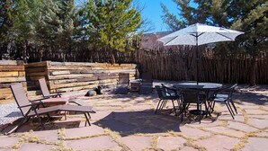 Eine Terrasse im Freien mit Steinboden, einer Holzbank, einem Tisch mit Stühlen und einem großen Sonnenschirm.