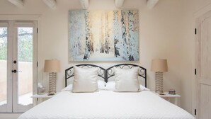 Quarto com uma cama grande, duas luminárias de cabeceira, um quadro sobre a cama e uma porta que dá para uma área externa.
