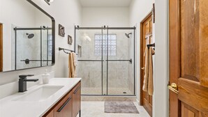Un baño moderno con ducha envuelta en vidrio, tocador de madera y un espejo grande.