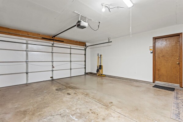 A garage with a concrete floor, a wooden door, and a yellow tool leaning against the wall.