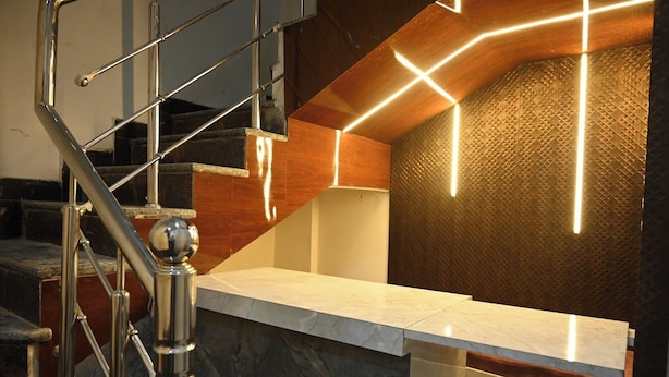 Un interior moderno con una escalera de mármol, un mostrador de recepción y una pared texturizada con iluminación geométrica.