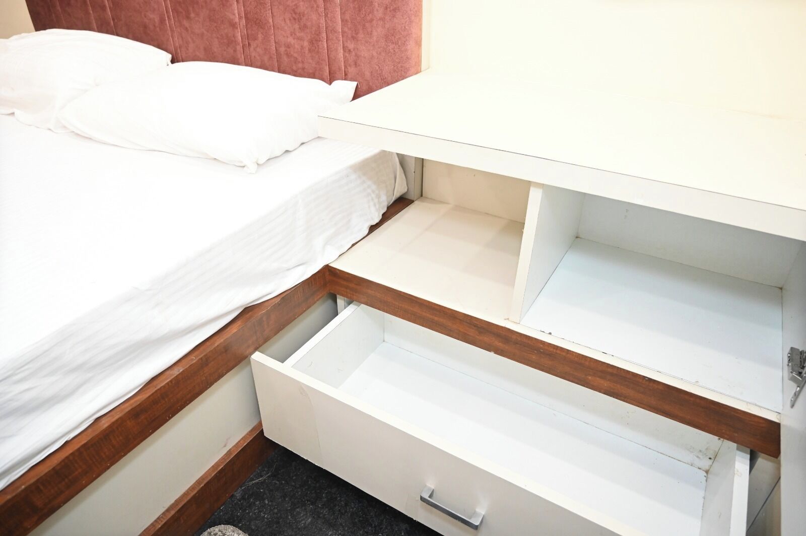 A bedroom with a bed, a wooden headboard, a white nightstand, and a white dresser with open drawers.