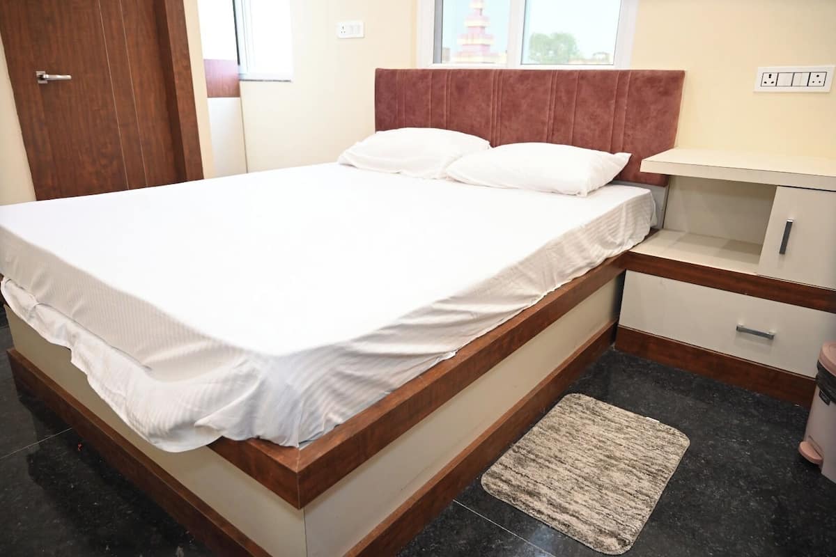 A neatly made bed with white linens, a wooden headboard, a bedside table with a lamp, and a small rug on a tiled floor.