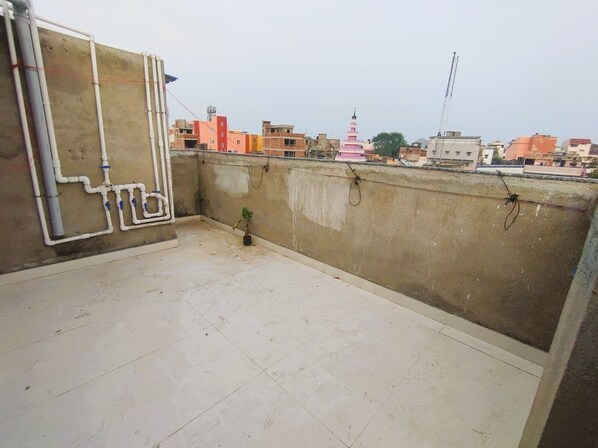 A rooftop terrace with a concrete floor, a potted plant, and visible plumbing pipes. - Hotel Royal Radiant (Ranchi)