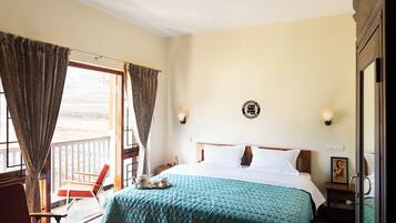 A bedroom with a bed, a chair, a table, and a balcony with curtains.