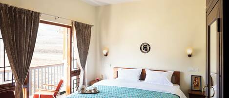 A bedroom with a bed, a chair, a table, and a balcony with curtains.