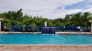 Una piscina rettangolare con una cascata al centro, circondata da una recinzione blu e piante in vaso.