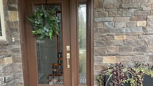 A brown door with a glass panel, a doormat with "welcome friends & family" text, and a planter with plants beside the door.