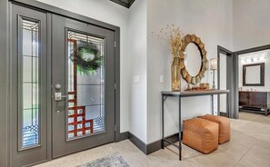 Un interior moderno con una puerta gris, un espejo decorativo y una consola con cojines.