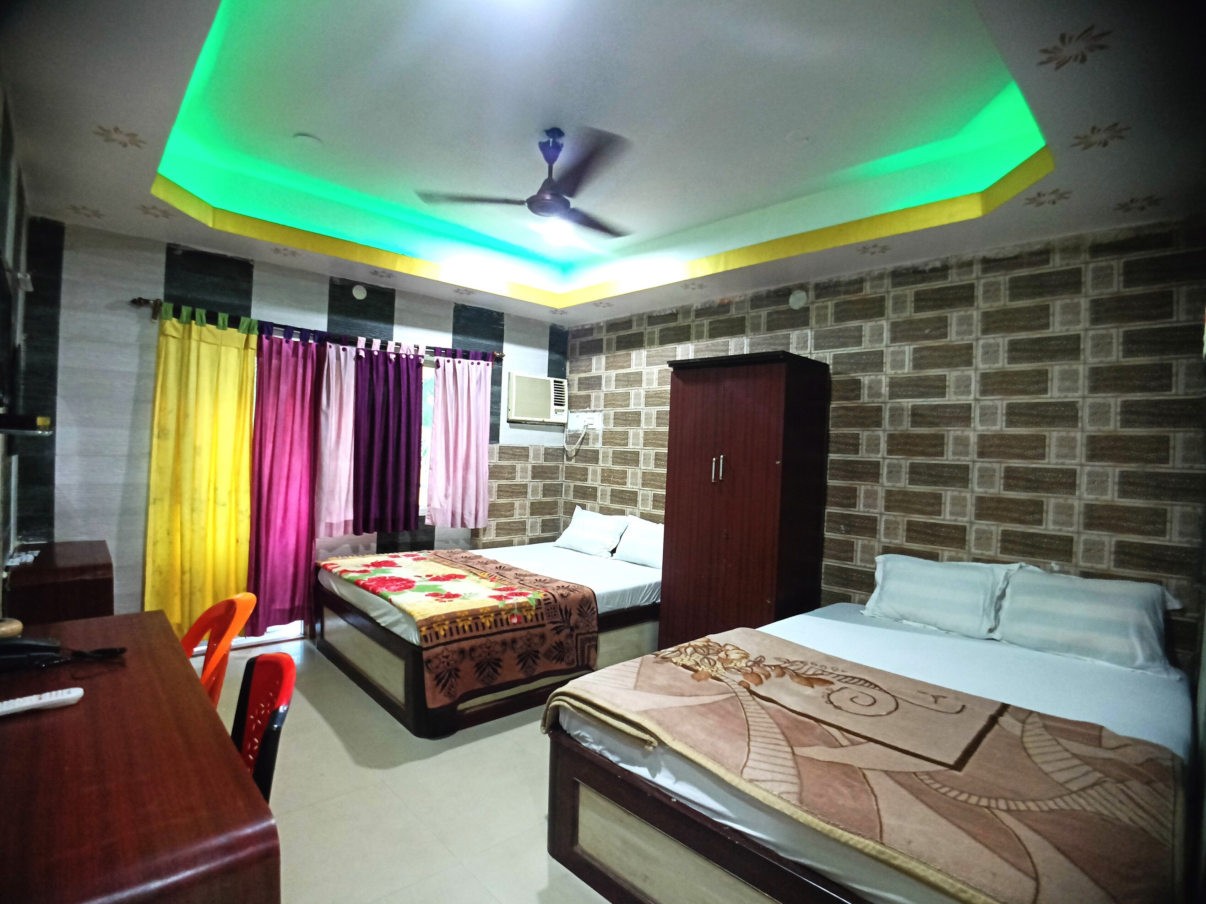 A hotel room with two beds, a desk, a chair, a wardrobe, and a ceiling fan.
