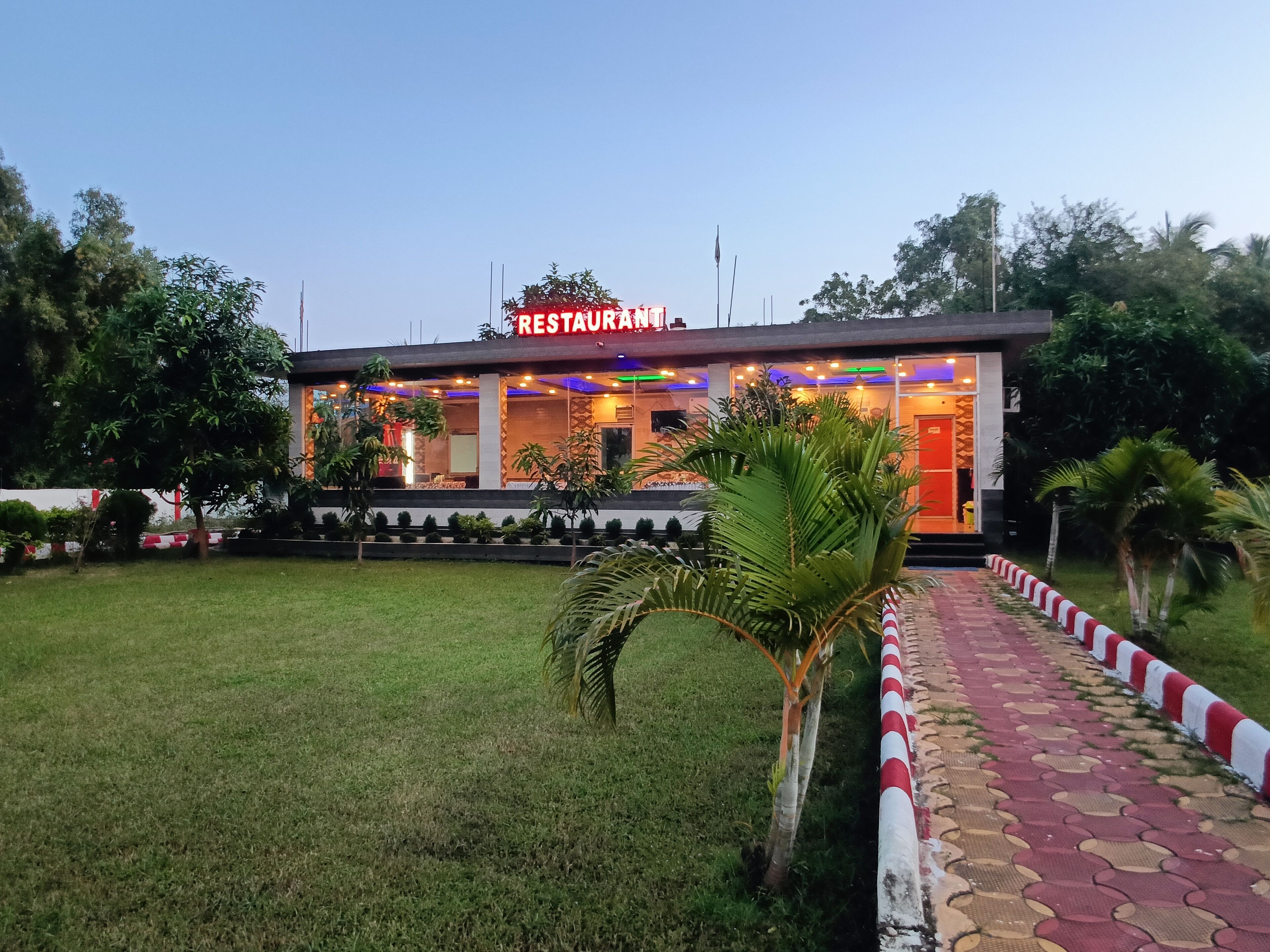 A restaurant with a sign, surrounded by greenery and a paved walkway.